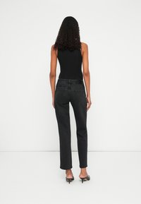 Body a coste nera abbinato a jeans neri a gamba dritta e in vita alta. Modella con eleganti tacchi neri. Sfondo minimalista.