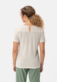 Top corto beige chiaro con maniche corte, scollatura rotonda e apertura a forma di chiave sul retro. Tessuto morbido, vestibilità casual, abbinato a pantaloni verdi.