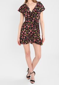 Vestido envolvente negro con mangas cortas y onduladas, que presenta un escote en V, un dobladillo con volantes y vibrantes patrones florales en rosa y amarillo.