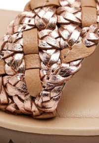 Sandalias trenzadas con una tira superior metálica en rosa dorado, que presentan detalles de cuero y una plantilla lisa en beige; diseño ligero y acolchado.