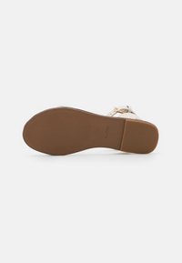 Béžová sandála s texturovanou hnědou gumovou podrážkou, s tenkým páskem kolem kotníku a malou zlatou sponou pro zapínání.
