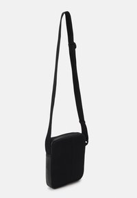 Borsa a tracolla nera con forma rettangolare strutturata, fronte in rete testurizzata e lati in pelle liscia, dotata di tracolla regolabile.