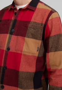 Punainen ja ruskea ruudullinen flanelli paita mustilla nappeilla ja yhdellä rintataskulla. Ominaisuuksiin kuuluu klassinen kaulus ja teksturoitu kangas.