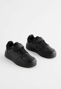Baskets noires en simili cuir avec une tige texturée, dotées de lacets et d'une sangle en Velcro pour un maintien sécurisé. Semelle en caoutchouc plate.