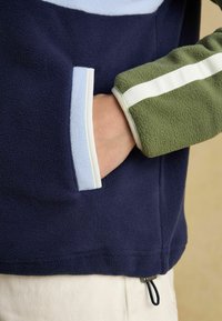 Fleece pulóver v námorníckej modrej, svetlomodrej a zelenej farbe, s prednou kapsou, žebrovanými manžetami a úchytom na leme.