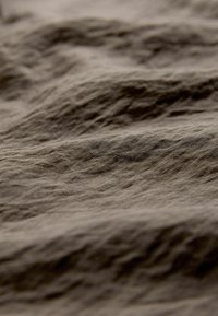 Tissu marron à surface texturée, présentant des plis doux et un aspect légèrement froissé, mettant en valeur sa qualité douce et légère.