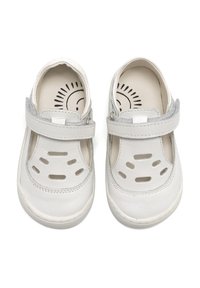 Zapatos de cuero blanco con diseños recortados en la parte frontal, que cuentan con una correa ajustable gris y una textura suave. Forro interior suave visible.