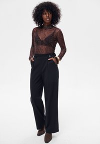 Brązowa przezroczysta bluzka z długim rękawem o wzorze skóry węża, zestawiona z czarnymi, szerokimi spodniami z wysokim stanem. Spodnie mają ozdobne guziki i boczne kieszenie.