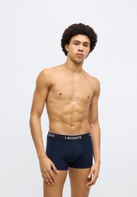 Boxer blu navy in tessuto morbido, con elastico in vita bianco con logo "LACOSTE". Texture liscia e design aderente.
