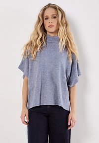 Himmelblauer,cropped Top mit einem hohen Kragen, kurzen Ärmeln und einem strukturierten Rippmuster. Kombiniert mit dunklen Jeans.