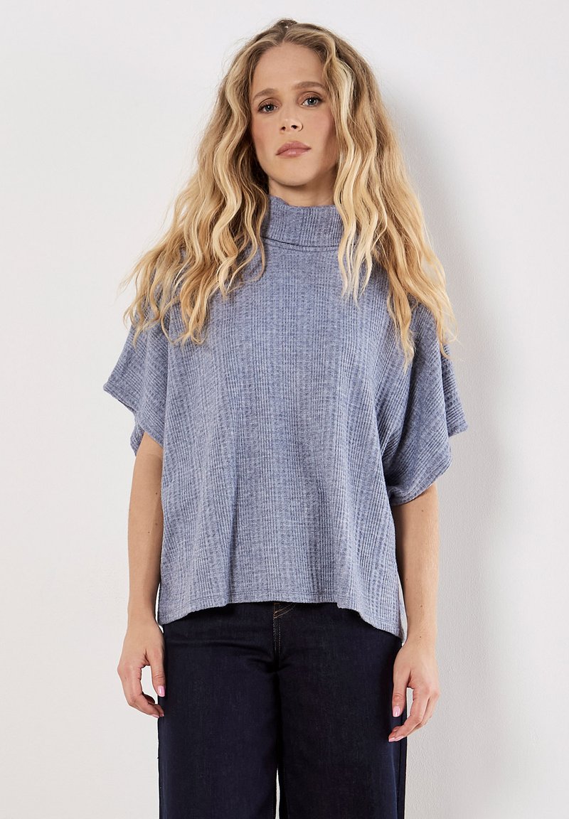 Himmelblauer,cropped Top mit einem hohen Kragen, kurzen Ärmeln und einem strukturierten Rippmuster. Kombiniert mit dunklen Jeans.