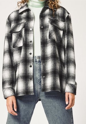 Chemise en flanelle à carreaux noir et blanc avec un devant à boutons, deux poches poitrine et une coupe décontractée. Portée par-dessus un col roulé vert menthe clair.