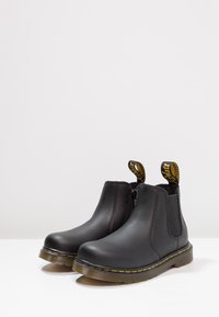 Black leather ankle boots with elastic side panels, yellow stitching detail, and signature pull tabs. Smooth finish with rubber soles.