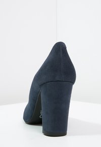 Marinblå mocka högklackad sko med spetsig tå och tjock klack. Slät textur med matt finish, som visar upp en minimalistisk design.