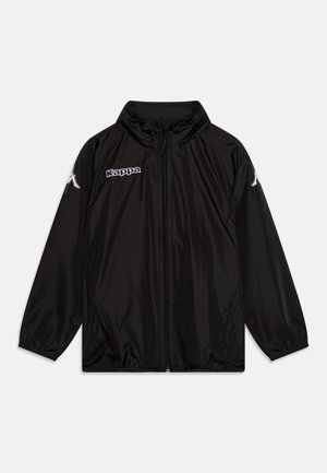 Casaco impermeável preto feito de material liso e leve. Possui uma gola alta, zíper completo, punhos elásticos e detalhe do logo na frente.