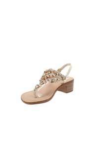 Sandal con tacco largo e cinturino trasparente, soletta beige e dettagli metallici. Presenta una parte superiore decorativa con strass e un design con fascetta tra le dita.