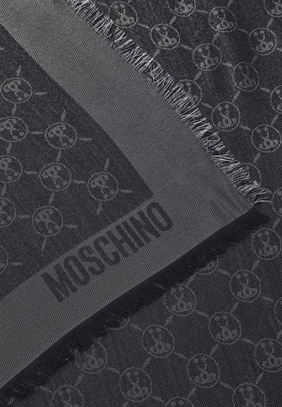 Černá šála s logem, která má texturovaný vzor s kruhovými motivy, třásněmi na okrajích a výraznou etiketou "MOSCHINO".