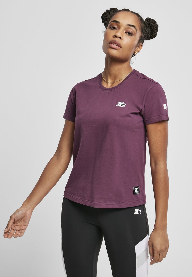 Tricou din bumbac violet cu guler rotund, mâneci scurte și un logo mic pe piept. Asortat cu colanți negri cu accente albe.