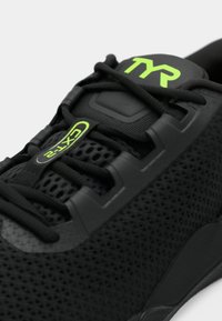 Zapatilla deportiva negra con parte superior de malla, acabado texturizado, acentos verdes y un prominente logo de TYR en la lengua. Presenta cordones elásticos y suela gruesa.
