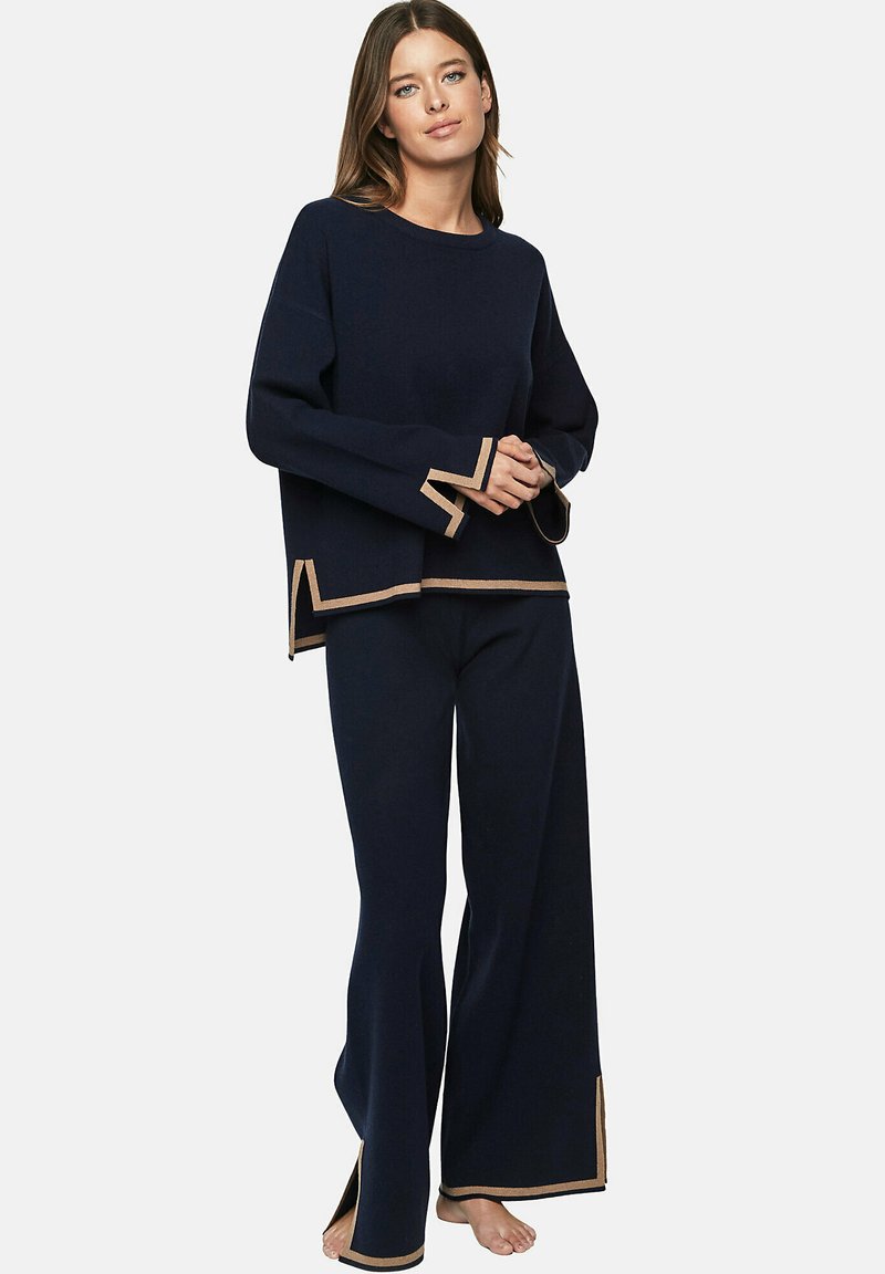 Ensemble de détente en tricot marine comprenant des manches longues, des fentes sur les côtés et une bordure beige contrastante au niveau des poignets et de l'ourlet. Pantalons à jambes larges inclus.