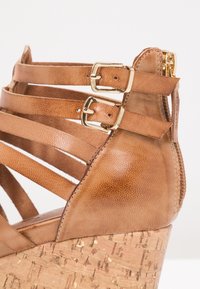 Sandale compensée en cuir marron avec plusieurs lanières en croix, boucles dorées et un talon en liège texturé.