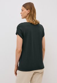 Haut court à manches courtes vert foncé avec des détails froncés sur les épaules, fabriqué en tissu doux, présentant une coupe décontractée et un col rond.