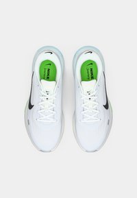 Λευκά αθλητικά παπούτσια με υφή στο πάνω μέρος, μαύρο λογότυπο Nike, πράσινη σόλα και μπλε λεπτομέρειες γύρω από το κολάρο και τη σόλα.