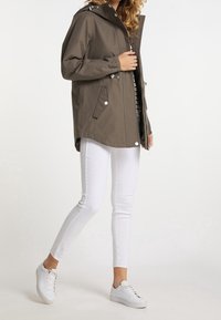 Veste marron imperméable avec capuche, poignets élastiques et poches avant, associée à un jean skinny blanc et des baskets blanches.