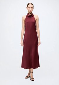 Robe en satin bordeaux à col licou drapé, corsage ajusté et jupe évasée fluide, associée à des sandales noires à brides.