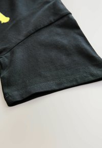 Schwarzes Baumwoll-T-Shirt mit Saum, der eine glatte Textur mit leichtem Stretch aufweist. Sichtbare Nähte entlang des Randes und gefaltete Ärmel-Details.