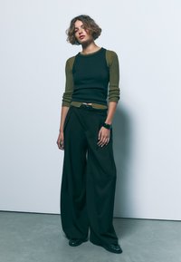 Črne široke hlače v kombinaciji s prilegajočo črno in olivno zeleno rebrasto majico. Obleka ima pas z naramnicami in gladko teksturo.