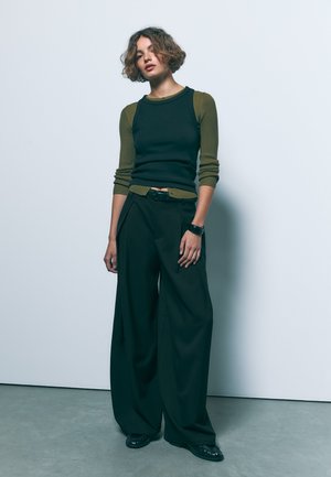 Černé široké kalhoty spárované s přiléhavým černým a olivově zeleným žebrovaným topem. Outifit má pásek v pase a hladkou texturu.