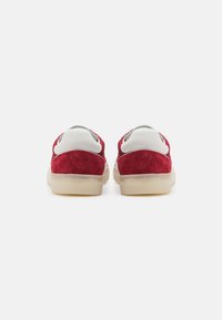Sneaker in suede rosso con dettagli in pelle bianca, design arrotondato e suole in gomma traslucida. Presenta dettagli grigi sul tallone.