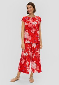 Rode top met bloemenpatroon, voorzien van plooien en korte mouwen, gecombineerd met bijpassende wijduitlopende broek. Heeft blauwe accenten en een relaxed fit.