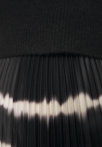 Ourlet de pull en maille noir au-dessus d'un tissu plissé noir et blanc avec un dégradé allant des tons foncés aux tons clairs.