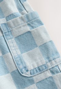 Tissu à carreaux bleu clair avec un motif quadrillé, présentant une texture douce et des coutures nettes le long des bords.