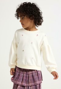 Kremowy sweatshirt z kwiatowym haftem, rękawami balonowymi i ściągaczami, zestawiony z teksturowaną spódnicą w fioletową kratkę.