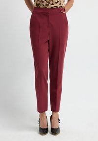 Woman wearing high-waisted burgundy tapered pants with a belt detail, paired with black pointed-toe heels and a leopard print top.