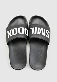 Zwarte slide-sandalen met een textuur matte afwerking, voorzien van een brede bovenband waarin het woord "SMILODON" in vette witte letters is gedrukt.
