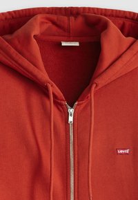 Felpa rossa con zip, interna testurizzata, con coulisse sul cappuccio e un piccolo logo Levi's sul lato sinistro del petto. Chiusura con zip in argento.