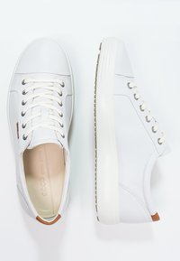 Weiße Ledersneaker mit runder Spitze, flachen Schnürsenkeln, gepolstertem Kragen und strukturiertem Gummisohl. Enthält eine kontrastierende braune Fersenschlaufe und dezentes Branding.