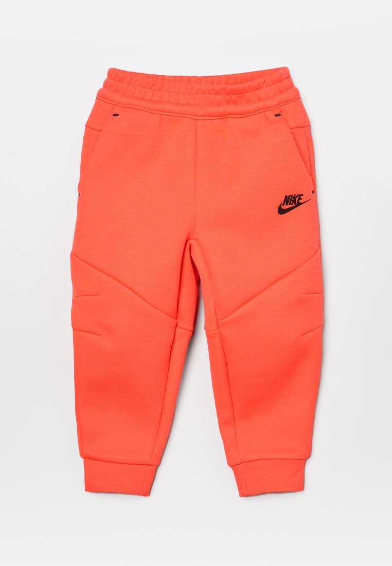 Joggery Nike w jasnym koralu, wykonane z miękkiego materiału, z elastyczną talią, bocznymi kieszeniami i czarnym logo z przodu.