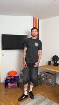 Camiseta cinza de mangas curtas com estampa gráfica no bolso, combinada com calções de ganga escuros. Ténis pretos com pormenores brancos e meias até ao tornozelo.