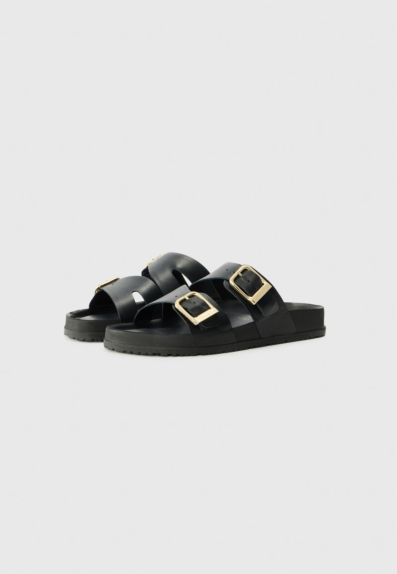 Schwarze Slidesandalen mit zwei breiten Riemen und goldenen Schnallen. Aus glattem synthetischem Material gefertigt, mit strukturierten Gummisohlen für besseren Halt.