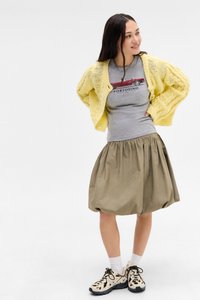 Yellow knitted cardigan, gray shirt with car graphic, beige skirt with gathered waist, and patterned sneakers with black soles.