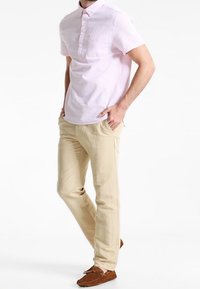 Košile s krátkým rukávem, světle růžová, s jemně strukturálním vzorem, v kombinaci s béžovými kalhotami a hnědými mokasínami.