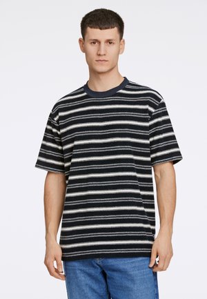 Camiseta de manga corta a rayas en blanco y negro con cuello redondo, hecha de una tela suave, usada con jeans de mezclilla azul.