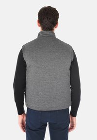 Gilet grigio intrecciato con colletto rialzato, design senza maniche e maniche nere in contrasto, indossato sopra pantaloni blu scuro.
