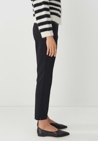 Zwarte op maat gemaakt broek met een slim fit, met een zijsplit aan de zoom. Gecombineerd met zwarte puntige flats en een zachte zwart-wit gestreepte trui.