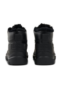 Sorte læderstøvler med blød pelsforing ved kraven, tekstureret ydre overflade og en robust gummisål med markante slidbaner.